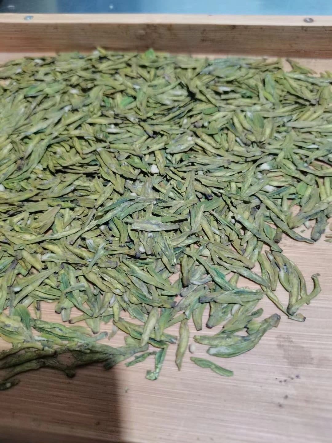 Flat, sword-shaped Longjing green tea leaves spread on a wooden tray