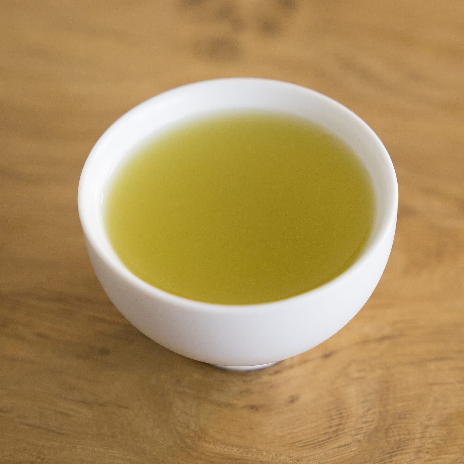 A white cup of clear, pale yellow-green sencha on a wooden table