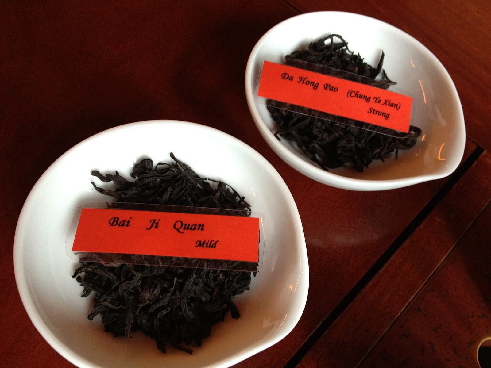 Two bowls of long, dark, twisted Wuyi oolong leaves labelled Da Hong Pao and Bai Ji Guan