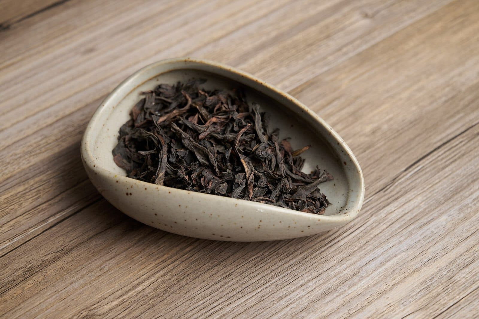 Dark brown twisted Wuyi oolong leaves in a ceramic tea scoop