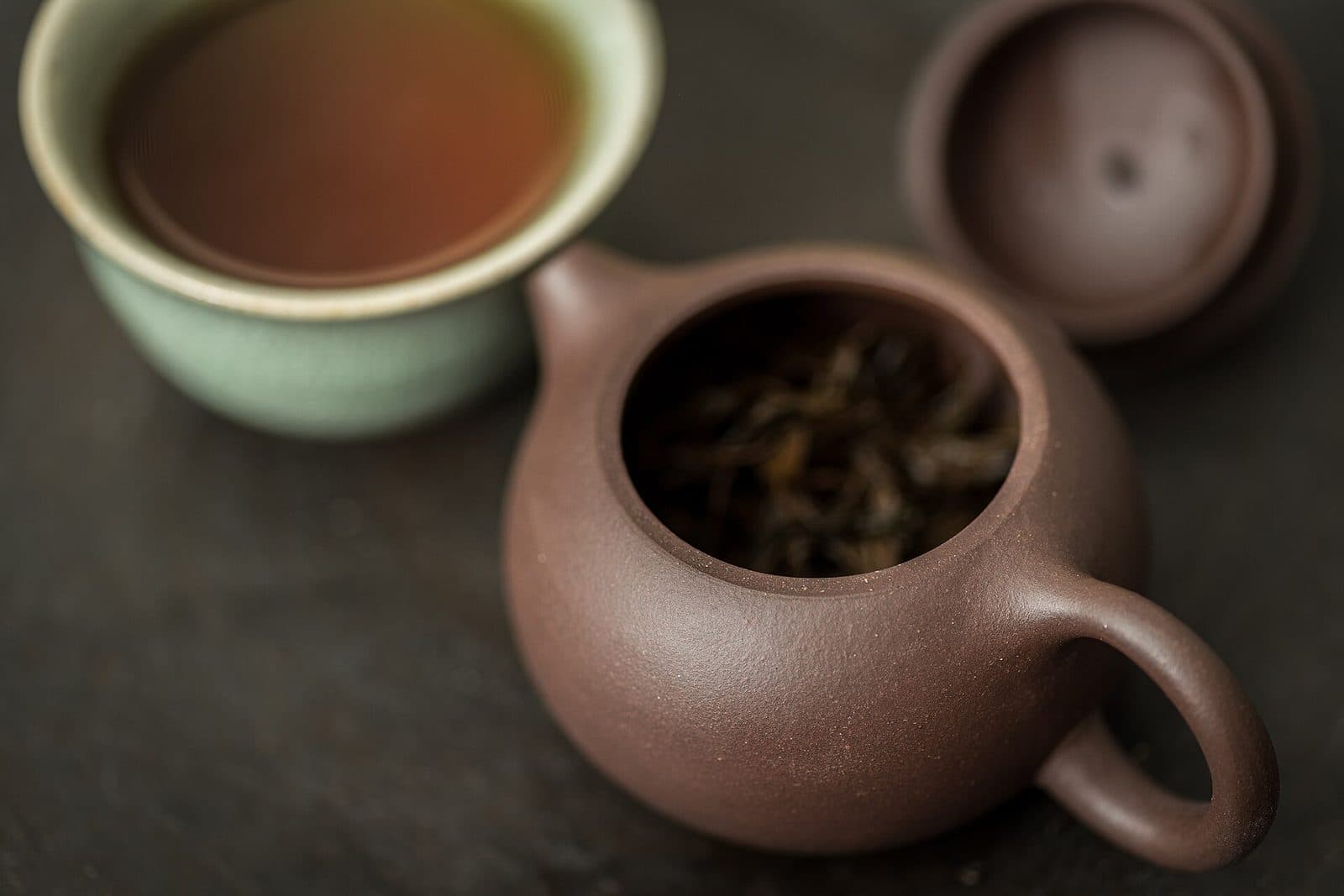 Unglazed Yixing clay teapot with tea leaves inside, beside a cup of tea